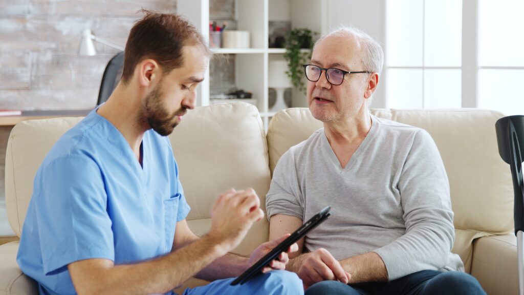 caucasian male nurse talking with nursing home patient about his health nurse is making notes digital tablet