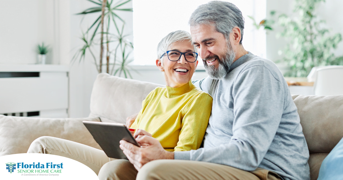 A senior couple smiles while looking at a laptop, showing how online resources can help family caregivers.