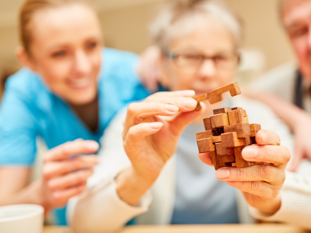 A caregiver helps a client stay active and engaged by using a burr puzzle, representing how dementia care services in Boca Raton can help seniors.