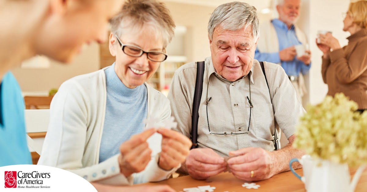 An older couple works on a puzzle with a caregiver, representing the kind of activity that helps those with dementia and also representing Alzheimer’s and Brain Awareness Month.