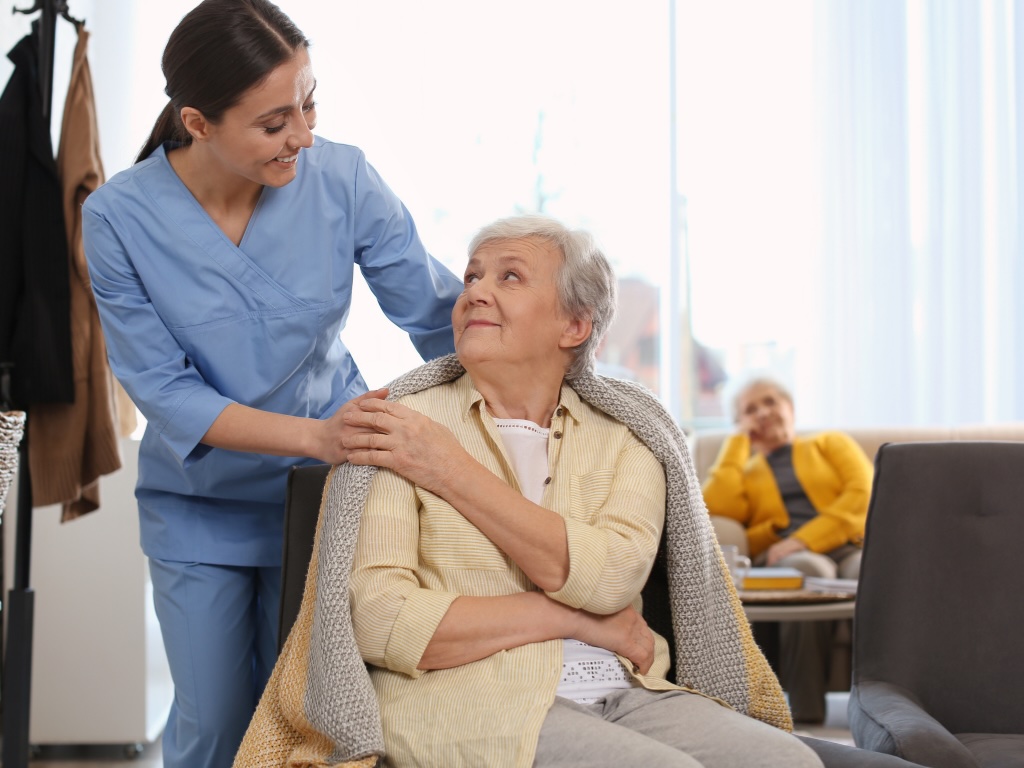 A caregiver wrapping an older adult in a blanket represents the type of care that geriatric care management can provide