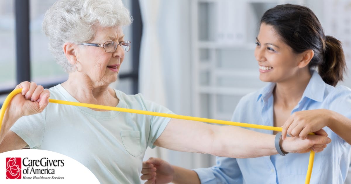 A woman helps an older woman exercise with a resistance band, showing how in-home physical therapy can help.