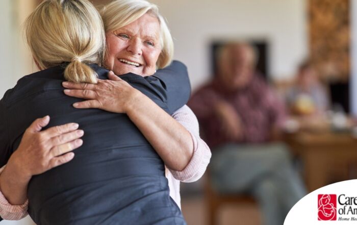 An older woman smiles as a younger woman visits her and hugs her, showing the effect that acts of kindness can have on senior loved ones.