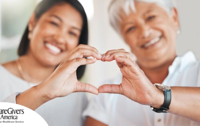 A daughter and an older mother create a heart with their hands, representing the feeling that is highlighted during National Family Caregivers Month