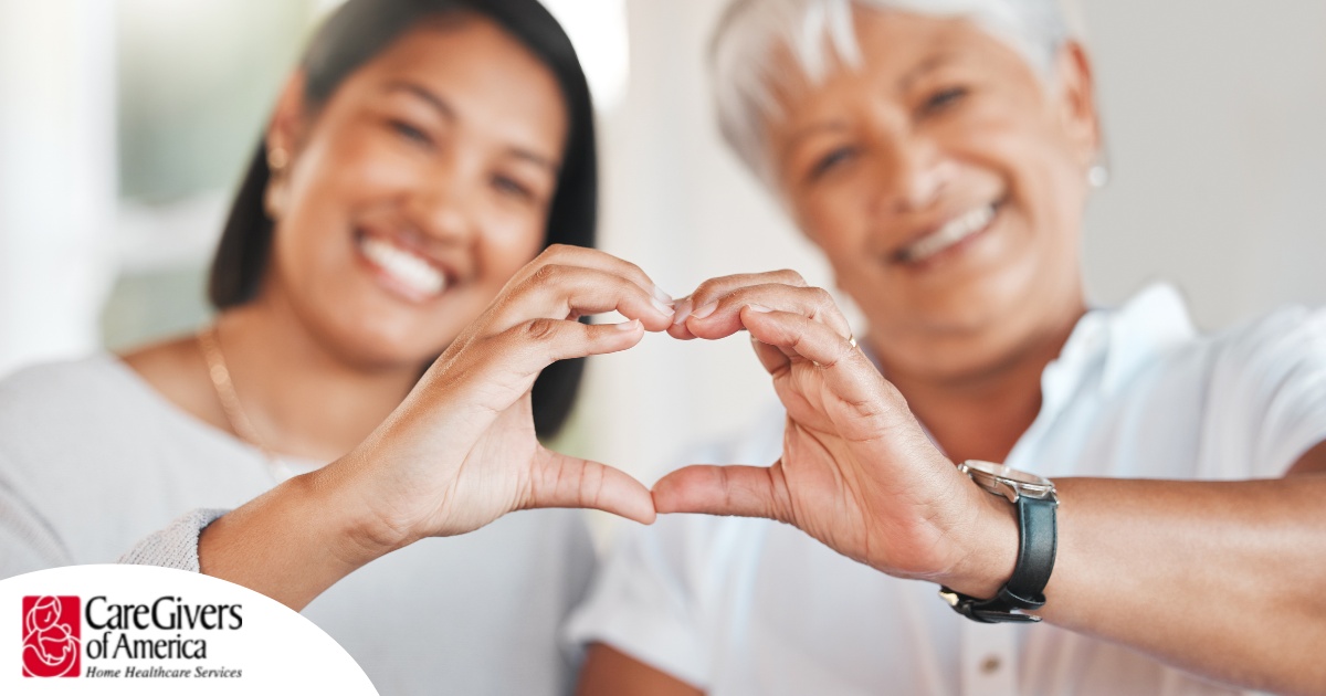 A daughter and an older mother create a heart with their hands, representing the feeling that is highlighted during National Family Caregivers Month