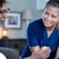 A nurse smiles as she helps an older couple with their medication in the comfort of their own home, showing the benefits of in-home nursing services.