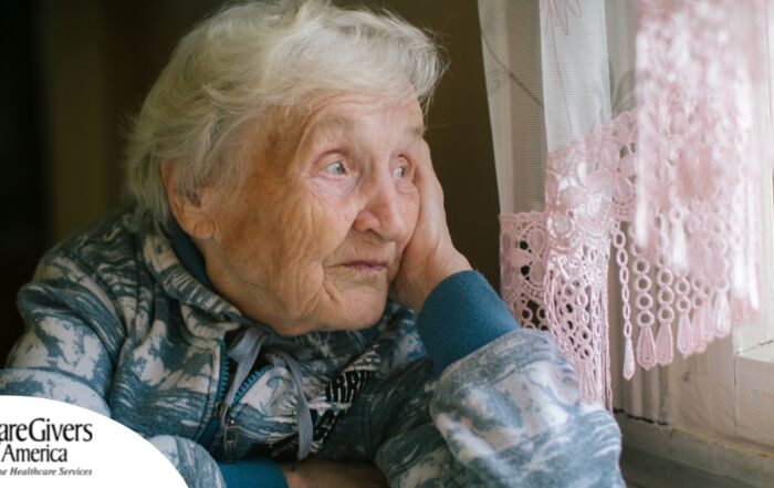 An older woman peacefully looks out of the window while the sun is still up, representing what can happen with sundowning.