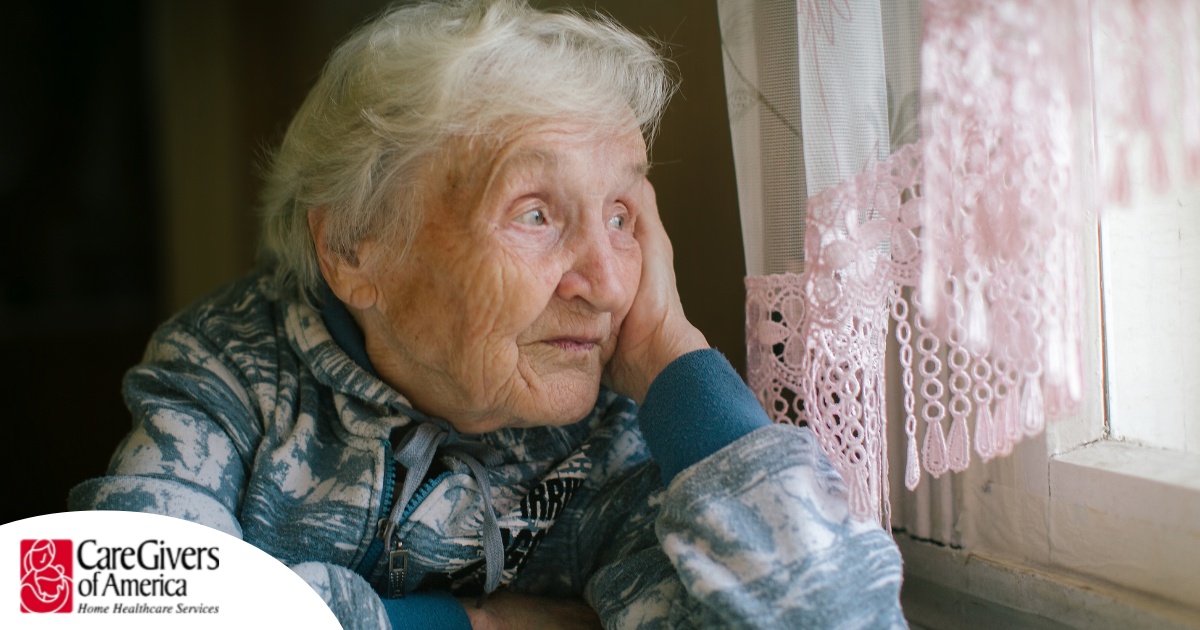 An older woman peacefully looks out of the window while the sun is still up, representing what can happen with sundowning.