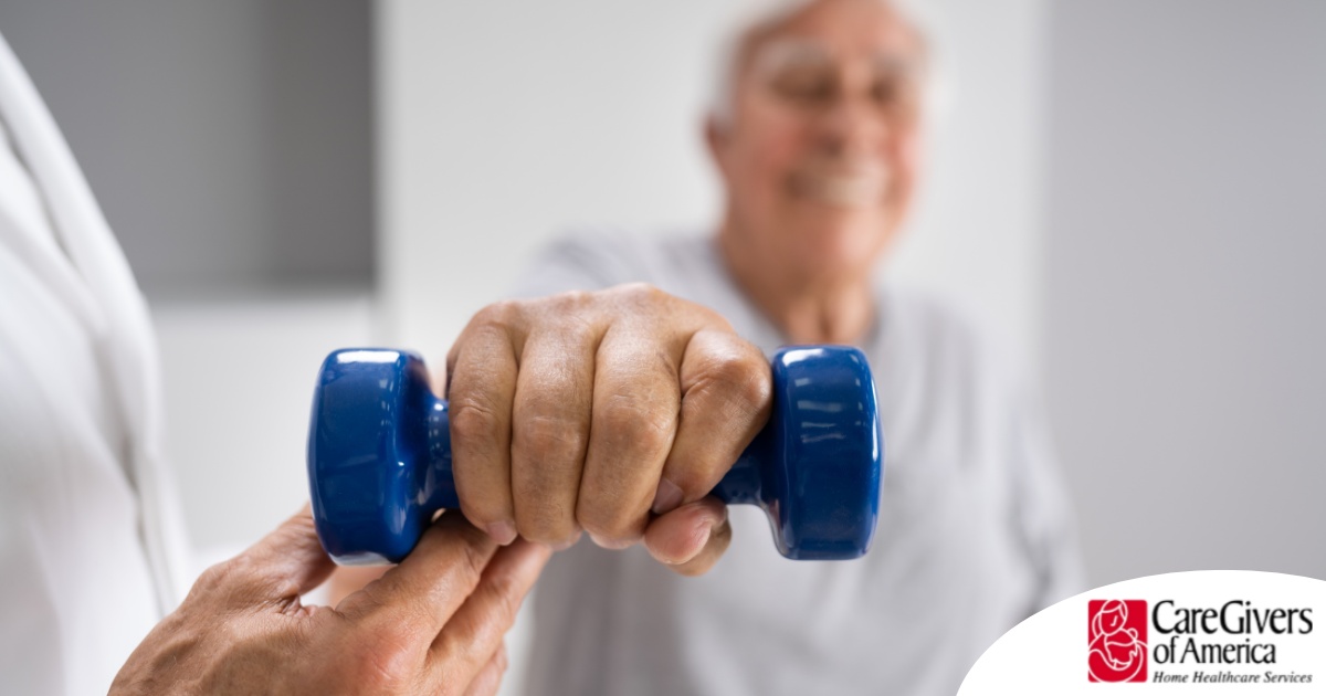 An older man is helped to lift a weight as part of physical therapy.