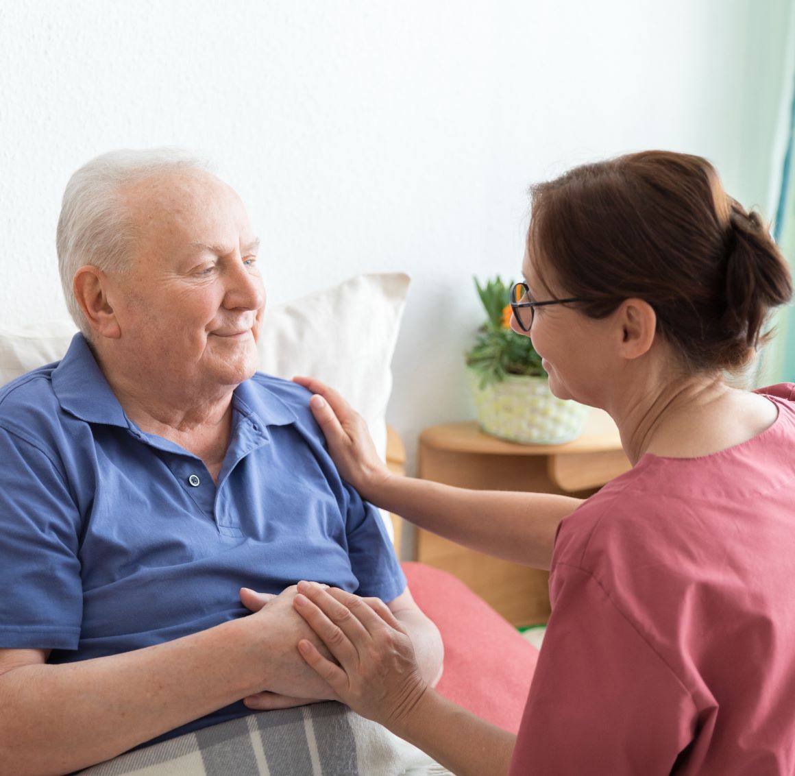 A care giver assists an elderly man who is lying in bed.