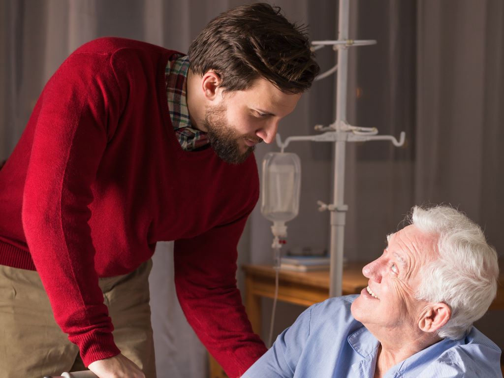 A care giver helping an elderly man in a hospital bed.