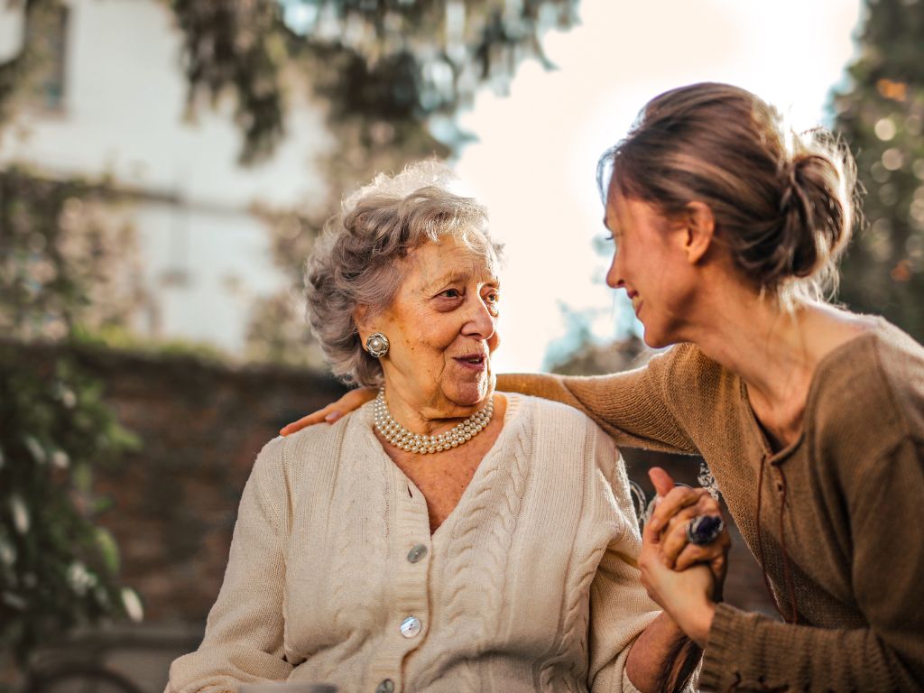 An cheerful elderly woman and a caregiver sit out side conversing. Companion Care in Cooper City