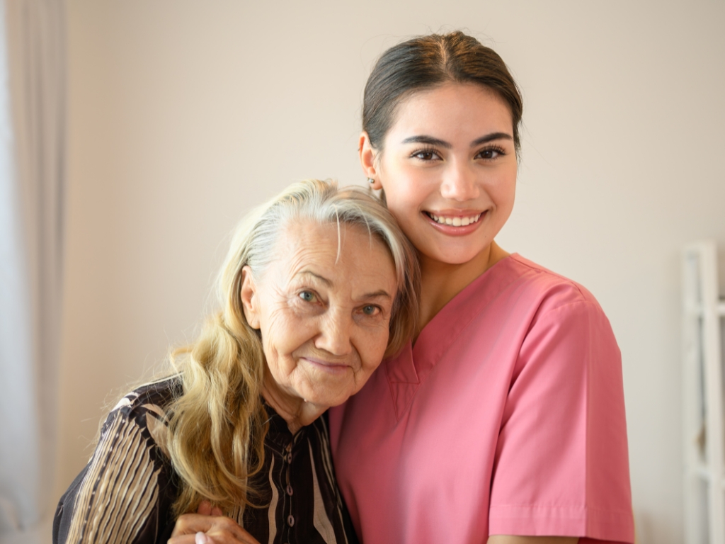 Excited young woman in a red t-shirt embracing a cute senior woman, both smiling and looking directly at the camera with joy.