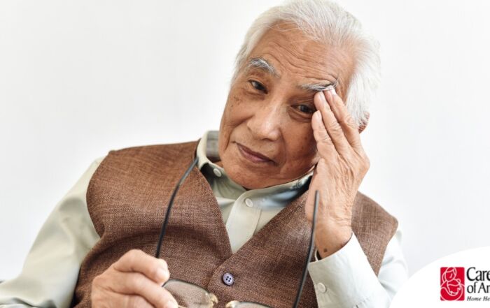 An older adult holds his head and his glasses representing vision problems like macular degeneration.