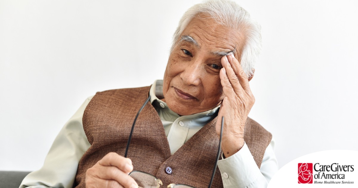 An older adult holds his head and his glasses representing vision problems like macular degeneration.