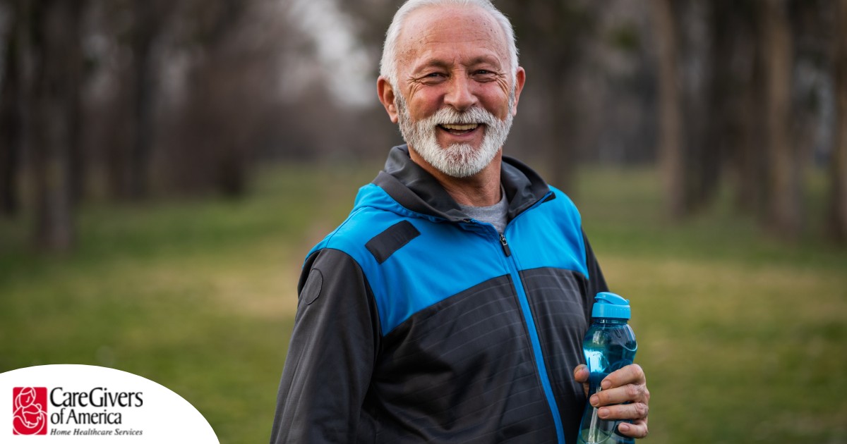 An older man smiles with a water bottle while exercising, representing the benefits of encouraging exercise when caring for seniors at home.