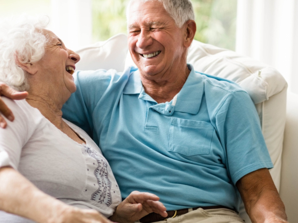 A senior couple sitting on a couch, laughing together in a cozy setting. For those seeking senior home care in Gulf Stream, moments like these emphasize the value of compassionate, personalized care at home.