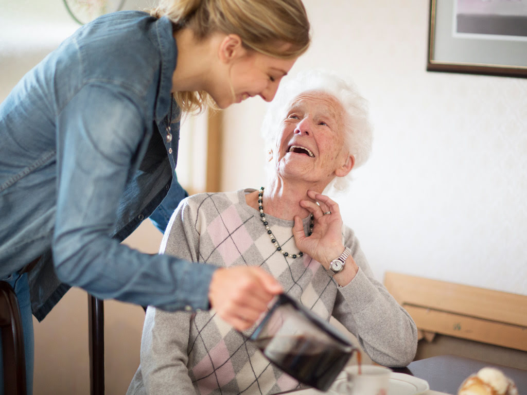 Senior woman in a wheelchair looking lovingly at a female caregiver by her side, highlighting their bond and the compassionate support provided through services like meal preparation.
