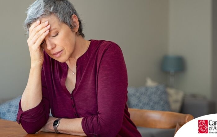 A woman holds her head in her hand, representing the stress that new family caregivers go through.