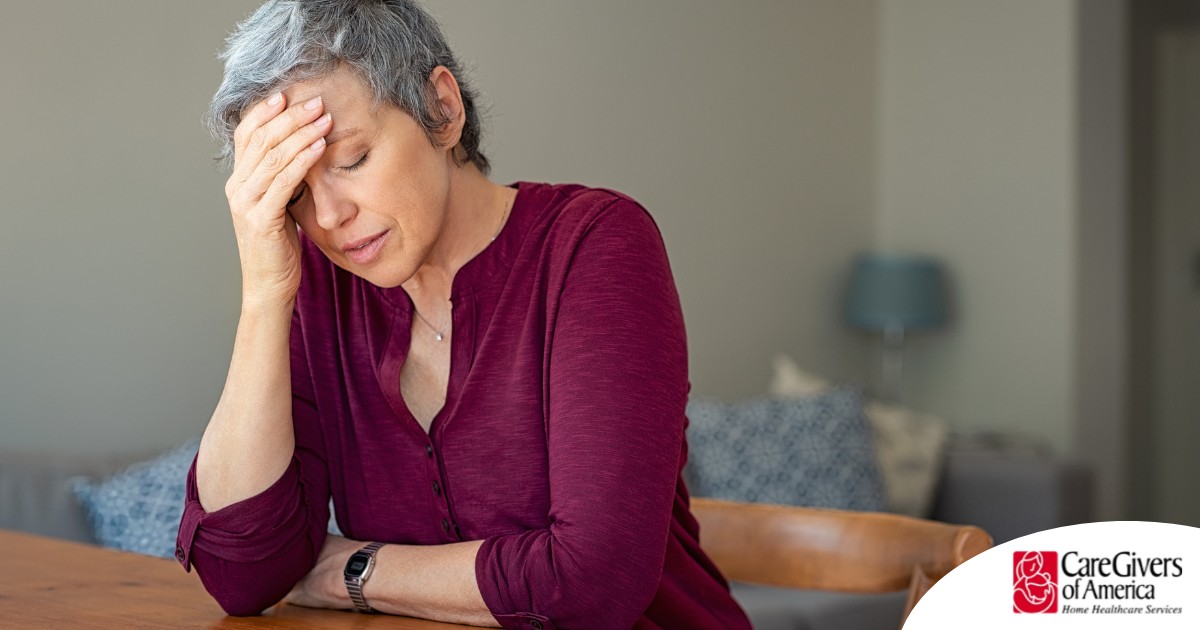 A woman holds her head in her hand, representing the stress that new family caregivers go through.