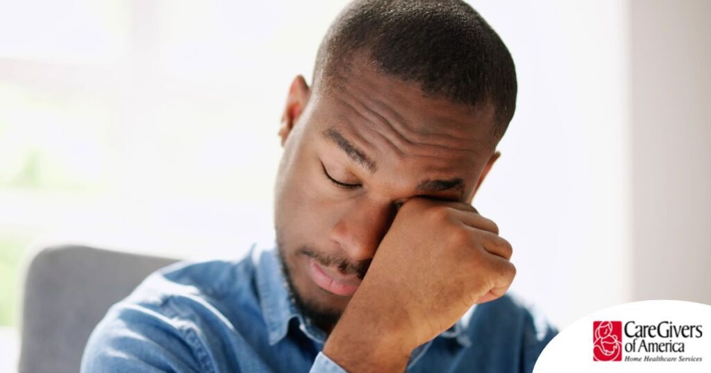 A man tiredly rubs his eyes, representing the exhaustion that can come with family caregiving.