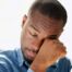 A man tiredly rubs his eyes, representing the exhaustion that can come with family caregiving.