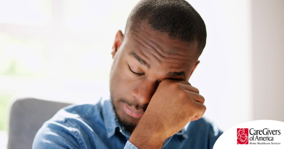 A man tiredly rubs his eyes, representing the exhaustion that can come with family caregiving.