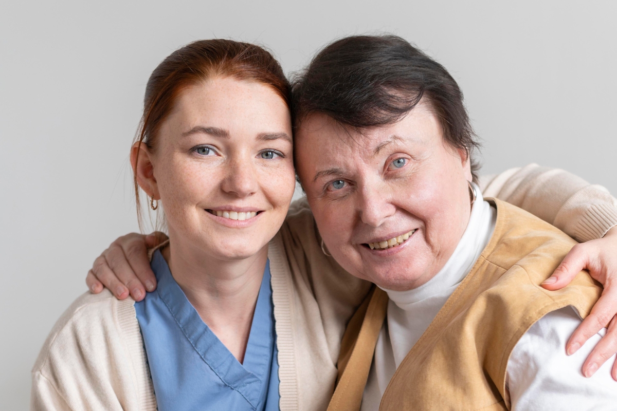 A smiling female caregiver with her arm around an elderly woman, both looking happy and close, symbolizing compassionate and personalized senior care in Jupiter Beach.