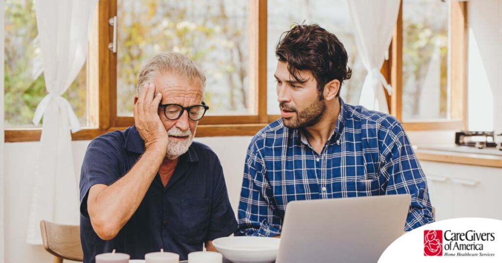 A man looks at a computer with his father who is confused, representing one of the early signs of dementia.