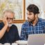 A man looks at a computer with his father who is confused, representing one of the early signs of dementia.