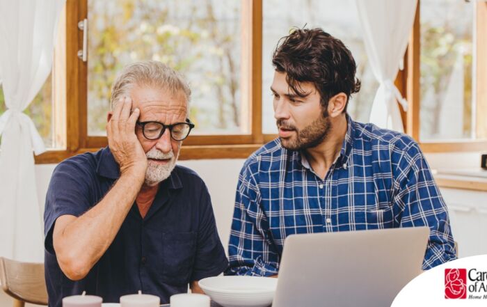 A man looks at a computer with his father who is confused, representing one of the early signs of dementia.