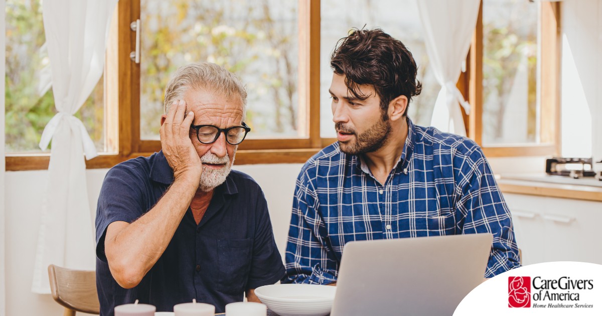 A man looks at a computer with his father who is confused, representing one of the early signs of dementia.