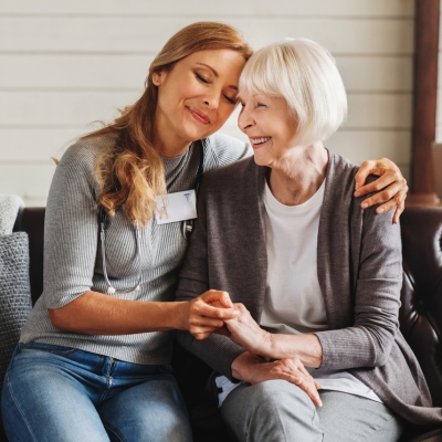 Female caregiver holding hands with a smiling senior woman, showing warmth, trust, and companionship in home care services.