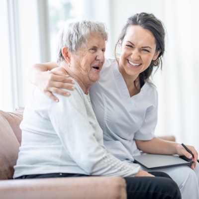 Companion Care in Coral Gables A cheerful caregiver sits close to a senior woman, offering support and companionship, representing the kindness and reassurance of companion care in Coral Gables.