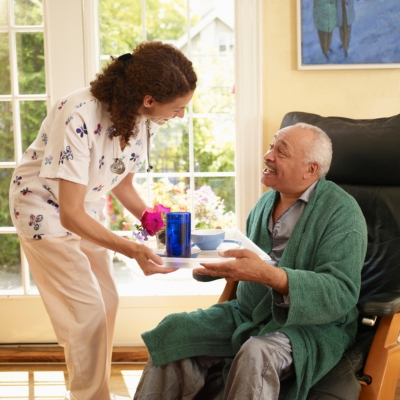 A caregiver brings a tray of food and water to an elderly man in a robe, highlighting the daily support and compassion offered by companion care in Oakland Park.