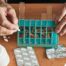 Older hands organize pills into a pill organizer, showing a great tool for managing medications.