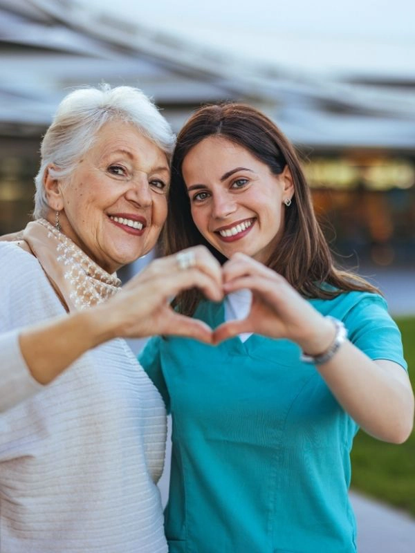 Smiling caregiver and older woman forming a heart shape with their hands, symbolizing compassionate home care services in Boca Raton by CareGivers of America.