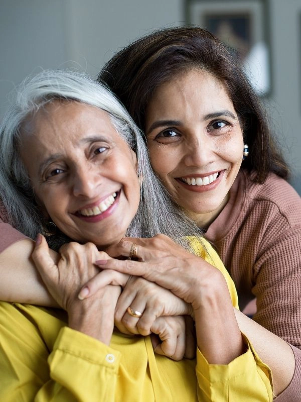Smiling caregiver embracing an older woman at home, representing the compassionate and personal care provided by CareGivers of America.