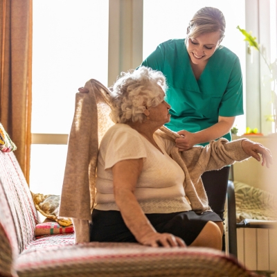 Caregiver helping an elderly woman with her sweater at home in High Point, providing comfort and companionship.