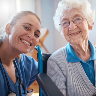 Compassionate caregiver smiling beside an elderly woman in a wheelchair, representing Alzheimer’s and Dementia Care in Palm Beach Gardens.