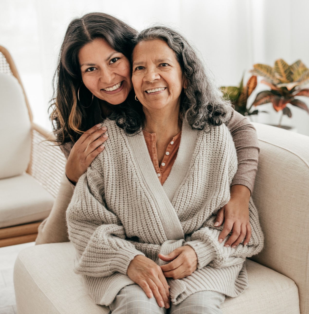 A smiling caregiver affectionately hugging a happy elderly woman in a cozy living room, illustrating dependable Alzheimer’s and dementia care in Margate, FL.