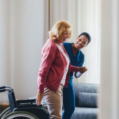 Fall Prevention in Margate (1) Caregiver helping a senior woman stand up from her wheelchair indoors, providing fall prevention support in Margate, FL