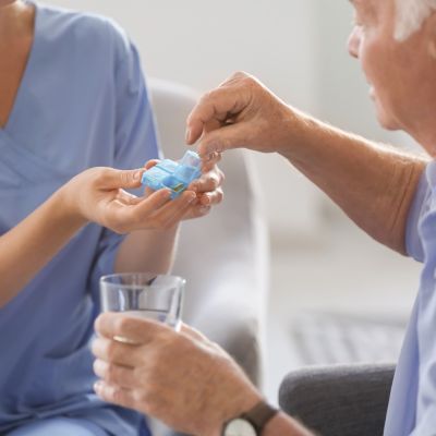 Caregiver providing medication supervision in Margate, helping a senior client with prescribed pills and a glass of water at home.
